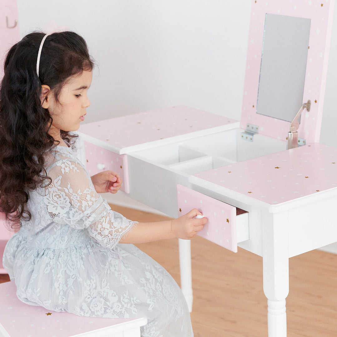 A little girl sitting and opening the drawers of the white and pink vanity table.