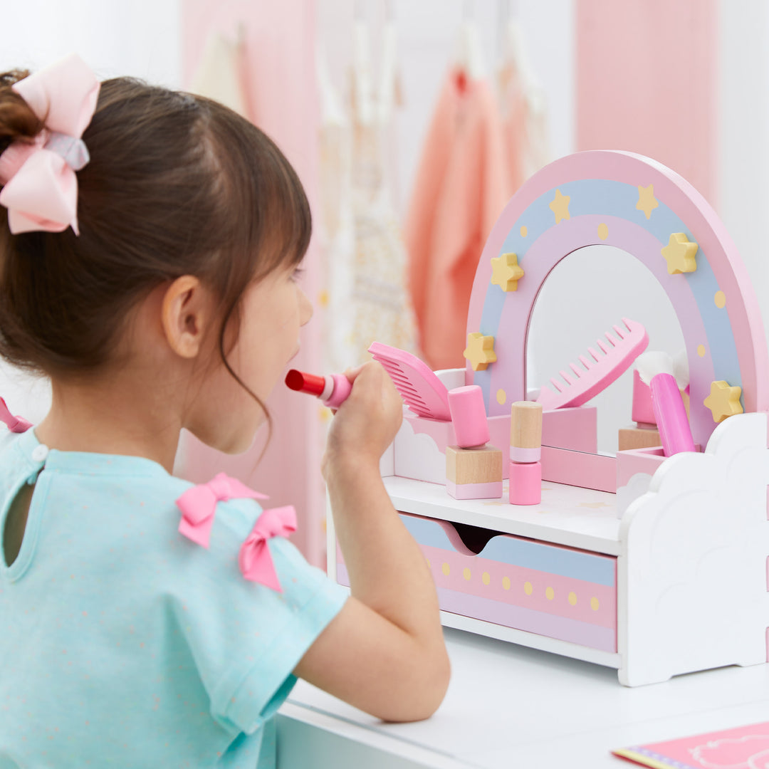 a little girl looking into the mirror of her white with rainbow accent tabletop vanity applying pretend lip stick.