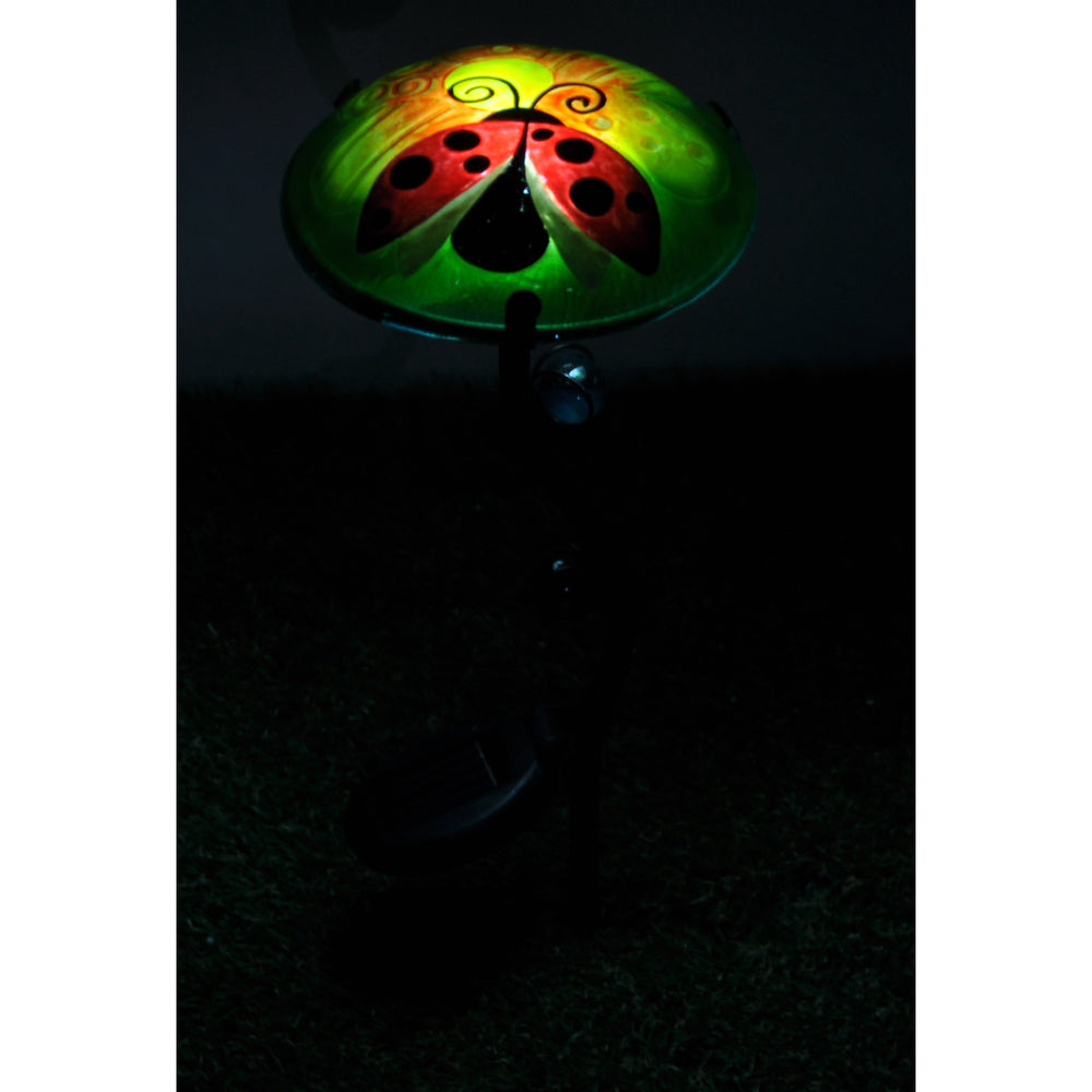 A fusion glass solar-powered light stake glowing at night, green with a ladybug and orange flower