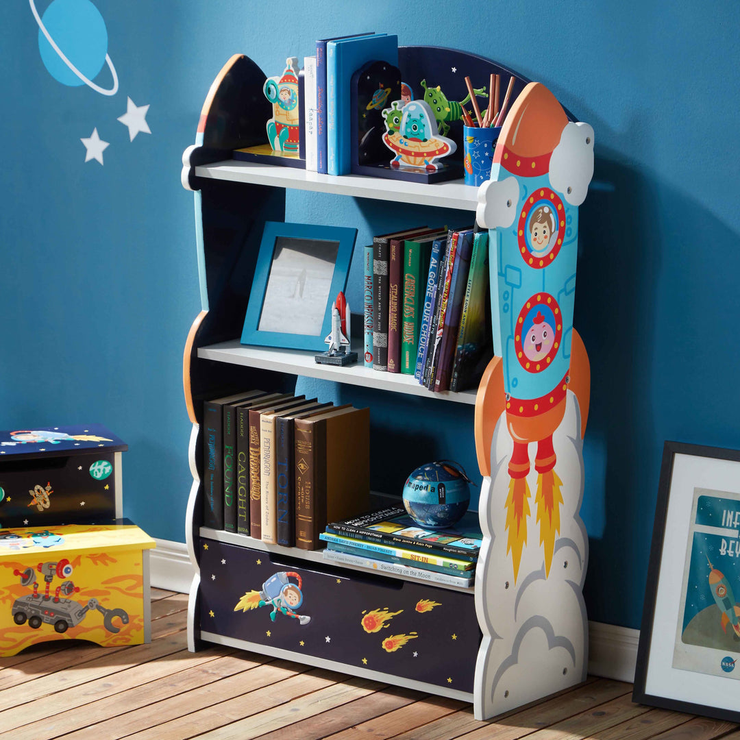 The Outer Space Bookshelf with Drawer with books and toys on the shelves against a blue wall.