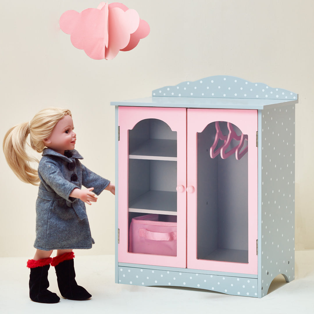 A doll is standing next to Olivia's Little World Polka Dots Princess Toy Closet with Hangers for 18" Dolls, Gray/Pink.