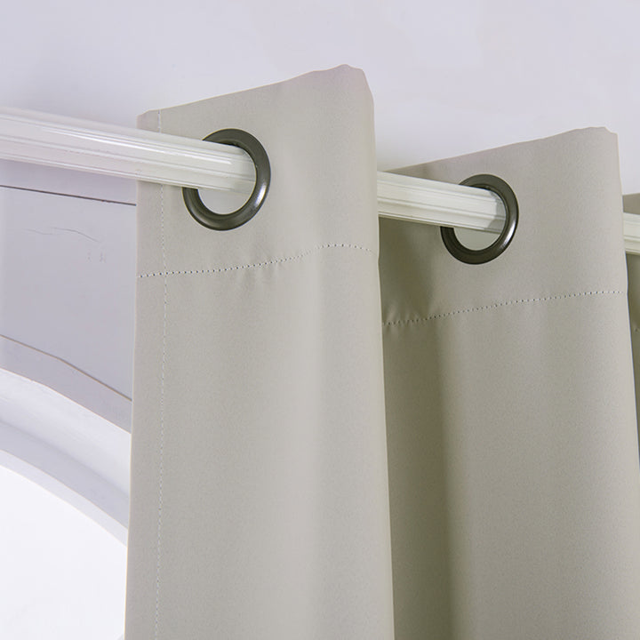 Beige polyester curtain panels with silver grommets hanging on a white curtain rod.