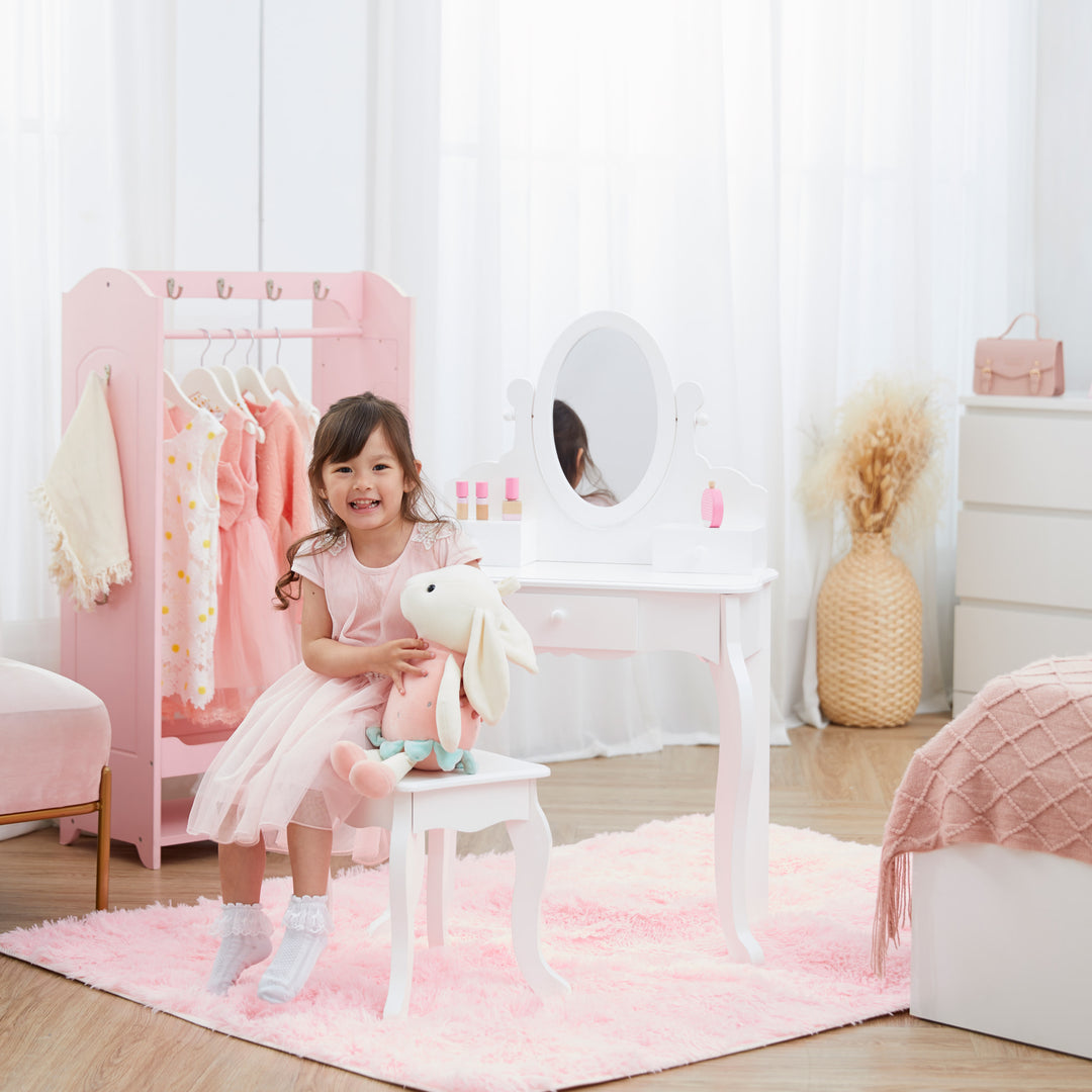 A girl with a stuffed bunny sitting on the stool of the white vanity playset with drawers and a mirror.