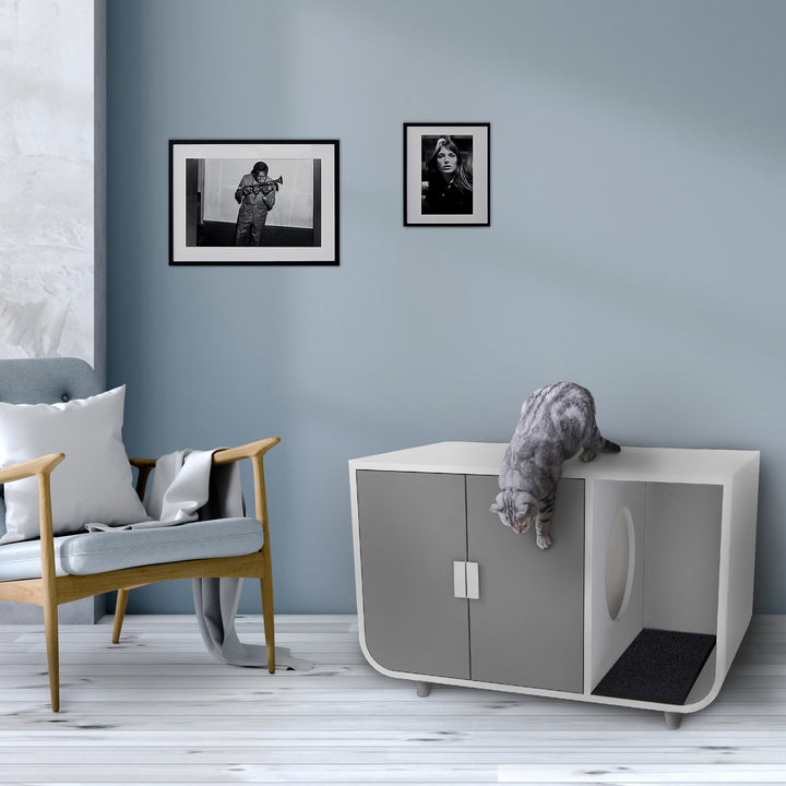 A cat exploring a Teamson Pets Large Dyad Wooden Cat Litter Box Enclosure and Side Table, Alpine White/Gray in a stylish living room with framed photographs on the wall.
