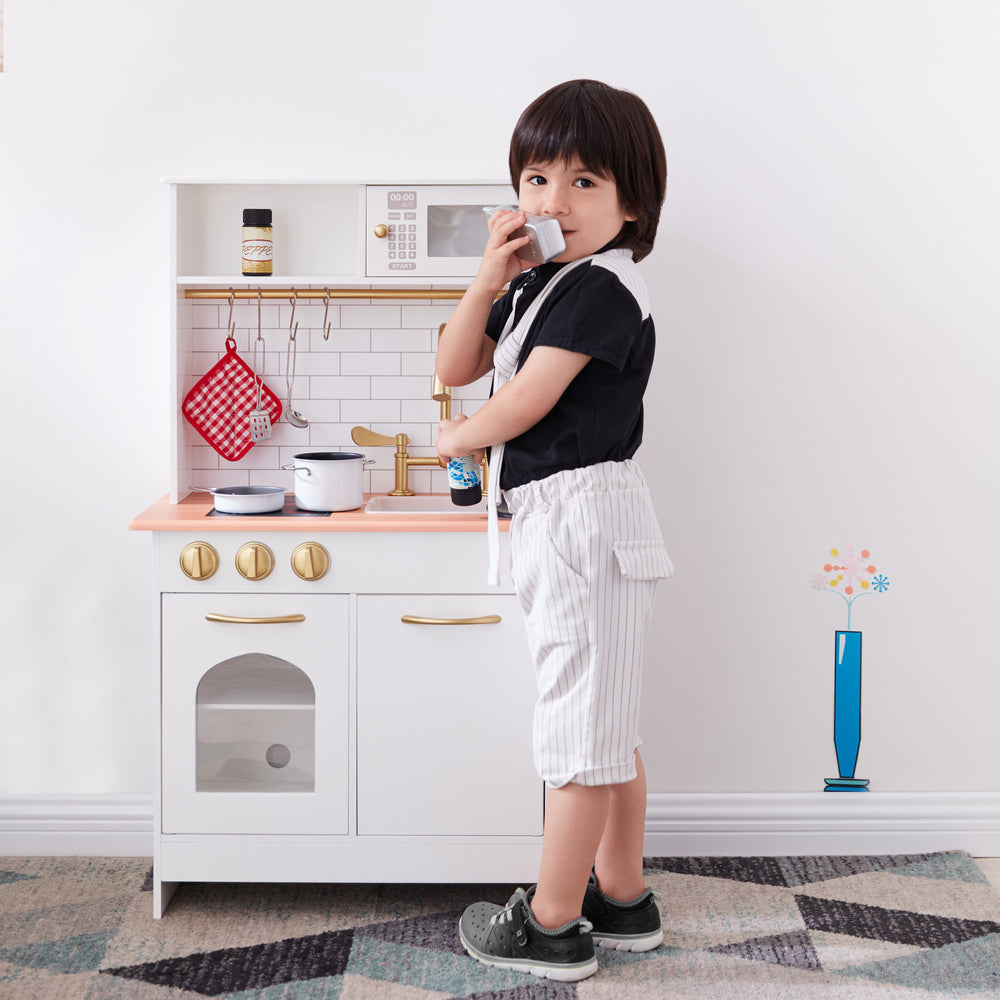 A child plays with a Teamson Kids Little Chef Boston Classic Play Kitchen & Cookware, White, pretending to talk into the pretend phone.