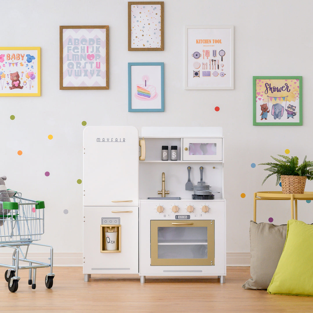 A child-friendly playroom with a Teamson Kids Little Chef Mayfair Classic Kids Kitchen Playset with 11 Accessories, White/Gold, colorful wall decorations, and a small shopping cart.