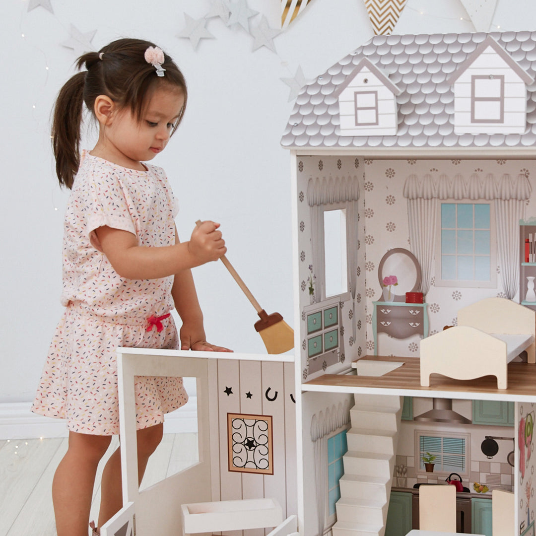 A little girl playing with the Teamson Kids Dreamland Farm Dollhouse with 14 Accessories, White/Gray.