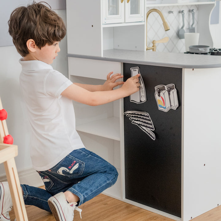 A little boy placing magnets on the magnetic panel of the modular play kitchen.