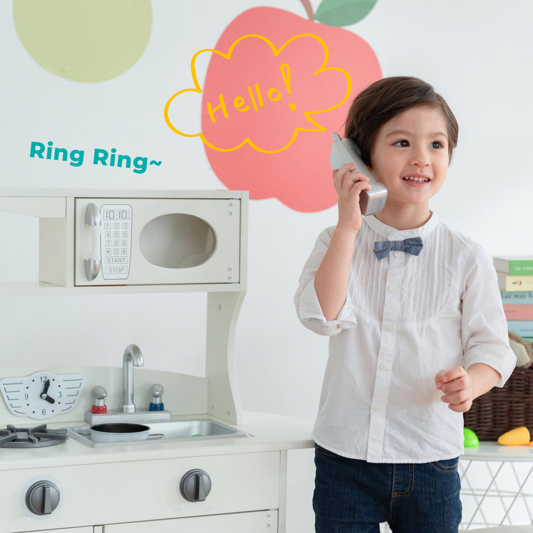 A young child playfully answers a toy telephone in the Teamson Kids Little Chef Westchester Retro Kids Kitchen Playset, Ivory.