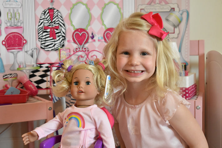 A little girl smiling next to her 18" blonde doll after shes finished her hair.