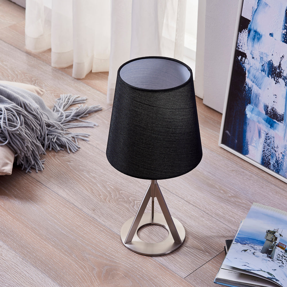 A Teamson Home Aria 15" Modern Table Lamp with Round Shade, Brass/Black on a wooden floor, serving as a stable light source.