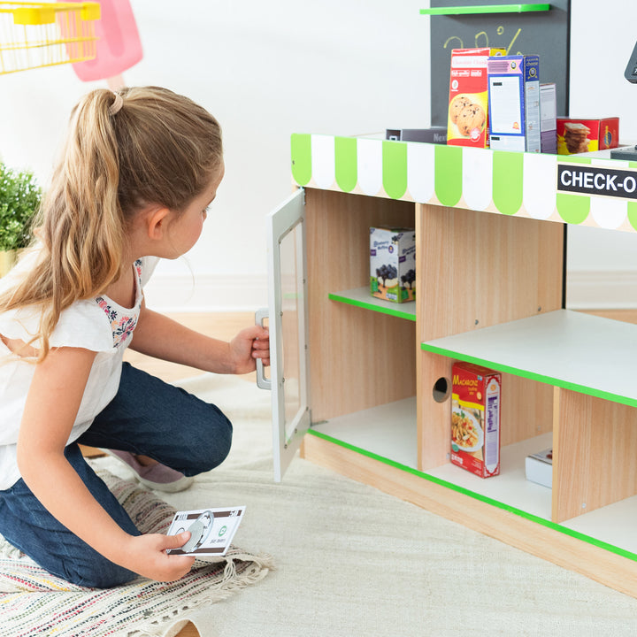 A child playing with a Teamson Kids Cashier Austin Play Market Checkout Counter with 26 Accessories at a market stand and pretend food products.