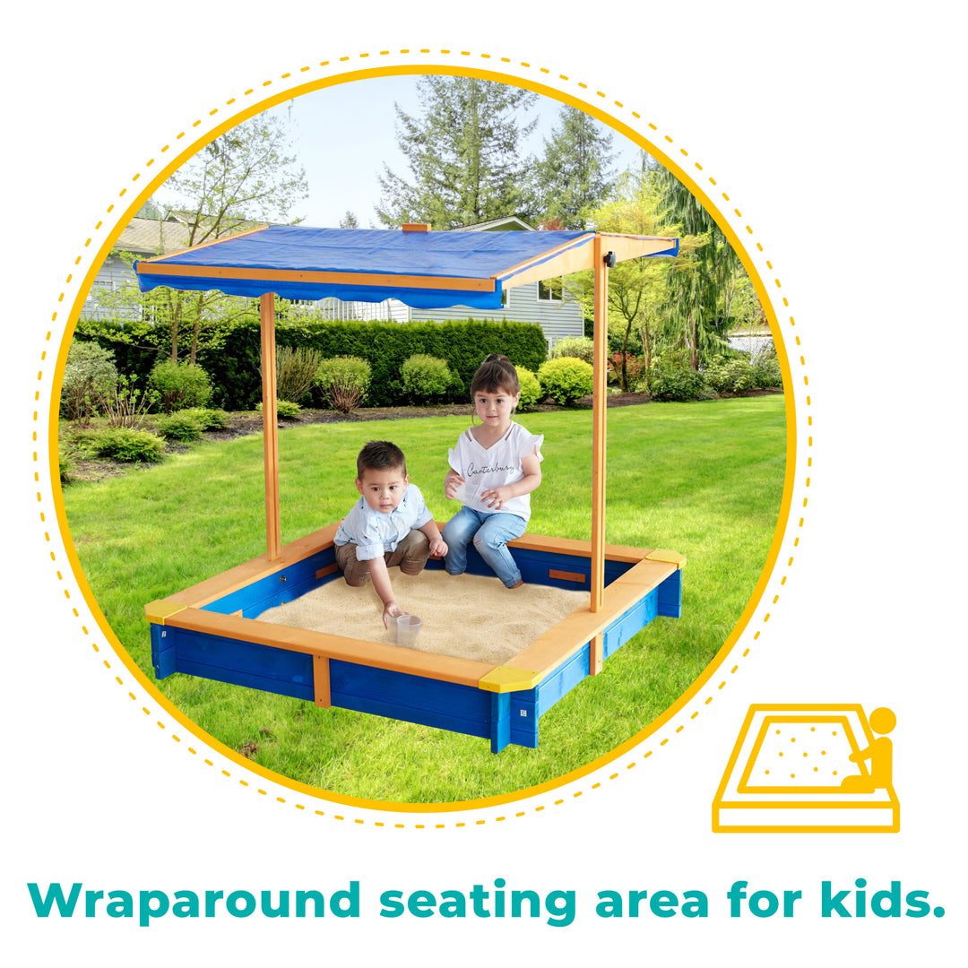 Two children playing in a Teamson Kids 4' Square Solid Wood Sandbox with Rotatable Canopy Cover, Honey/Blue with built-in seats and a canopy.