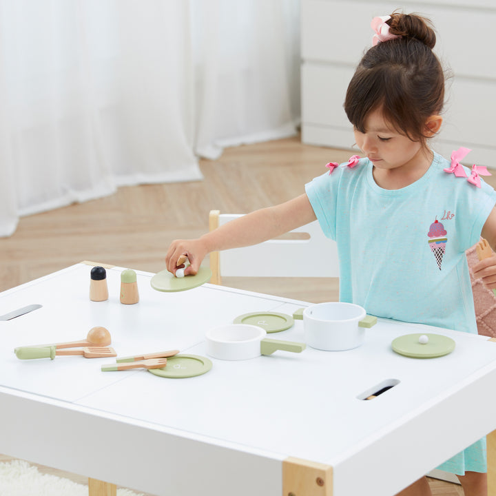 A young girl enjoying a kids play session with a Teamson Kids Little Chef Frankfurt Wooden Cookware Play Kitchen Accessories, Green on a white table.