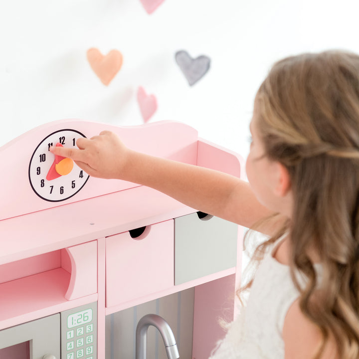 A child adjusting a play clock on a pink Teamson Kids Little Chef Florence Classic Play Kitchen.