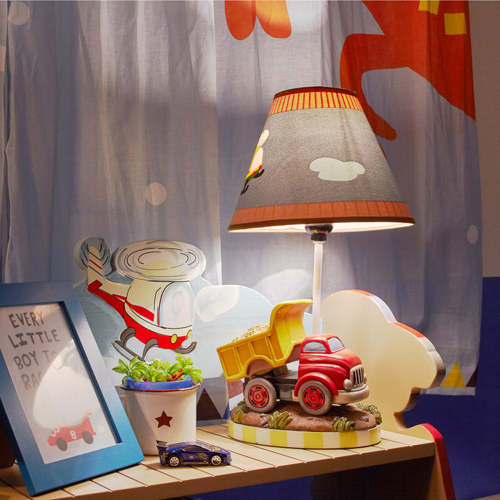 A picture of the dump truck table lamp on a dresser next to a curtain with a helicopter on it.