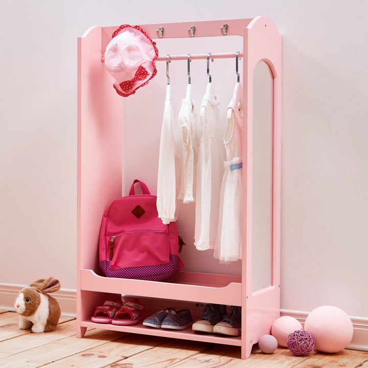 Pink wardrobe white dresses hanging, a white and red bonnet, a pink bookbag, and shoes on the bottom shelf.