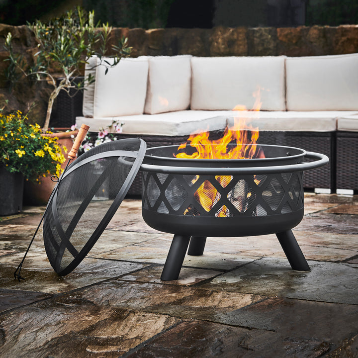 A Teamson Home 30" Outdoor Round Wood Burning Fire Pit with a protective mesh screen and a steel base set on a stone patio, perfect for outdoor decor.
