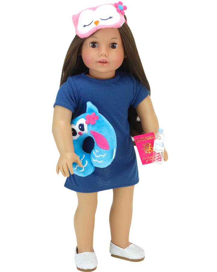An 18" brunette doll stands with an owl sleep mask pulled up on her head, while she holds an owl travel pillow, bottle of water and passport.