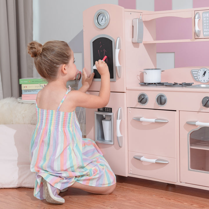 Young girl playing with a Teamson Kids Little Chef Westchester Retro Play Kitchen, Pink, complete with a toy telephone and interactive features.