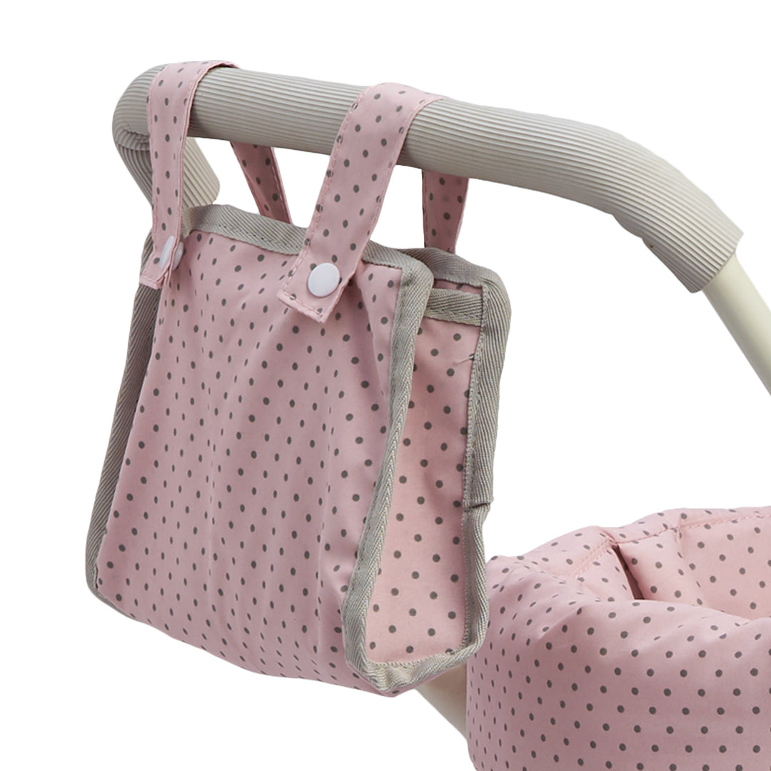 A close up of the removable diaper bag with snaps hanging from the handle of the baby buggy, pink with gray polka dots.