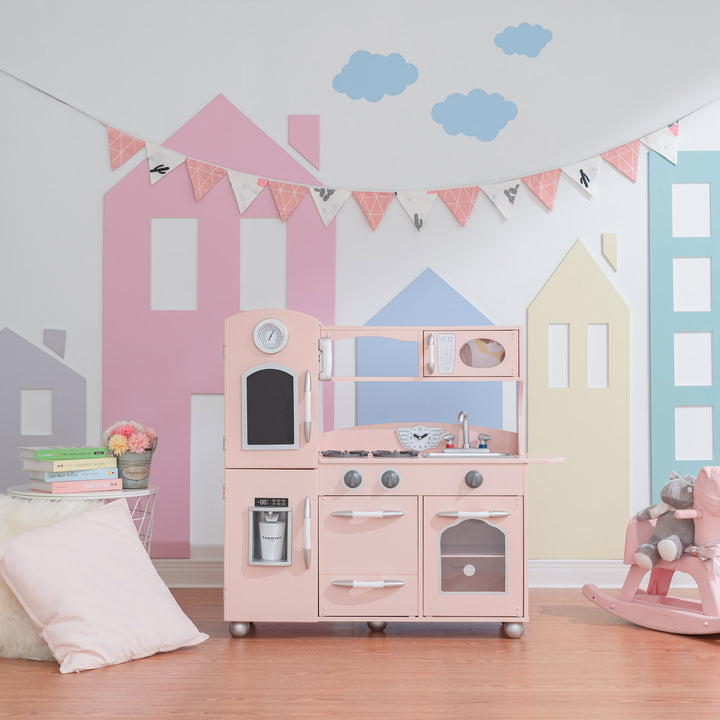 A child's playroom with a Teamson Kids Little Chef Westchester Retro Play Kitchen in Pink, complete with interactive features, and wall decorations resembling a quaint town.