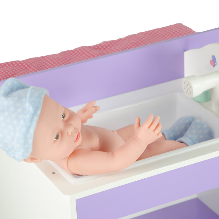 A close-up of a baby doll sitting in the sink portion of the baby doll changing station.