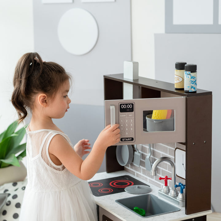 A young girl playing with a Teamson Kids Little Chef Burgundy Classic Play Kitchen, Expresso/Black set, featuring interactive features.