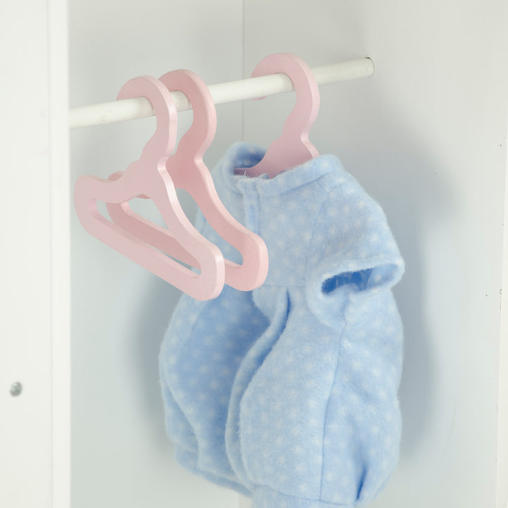 A close-up of the closet portion of the baby doll changing station with three pink hangers and a blue baby doll jumper.