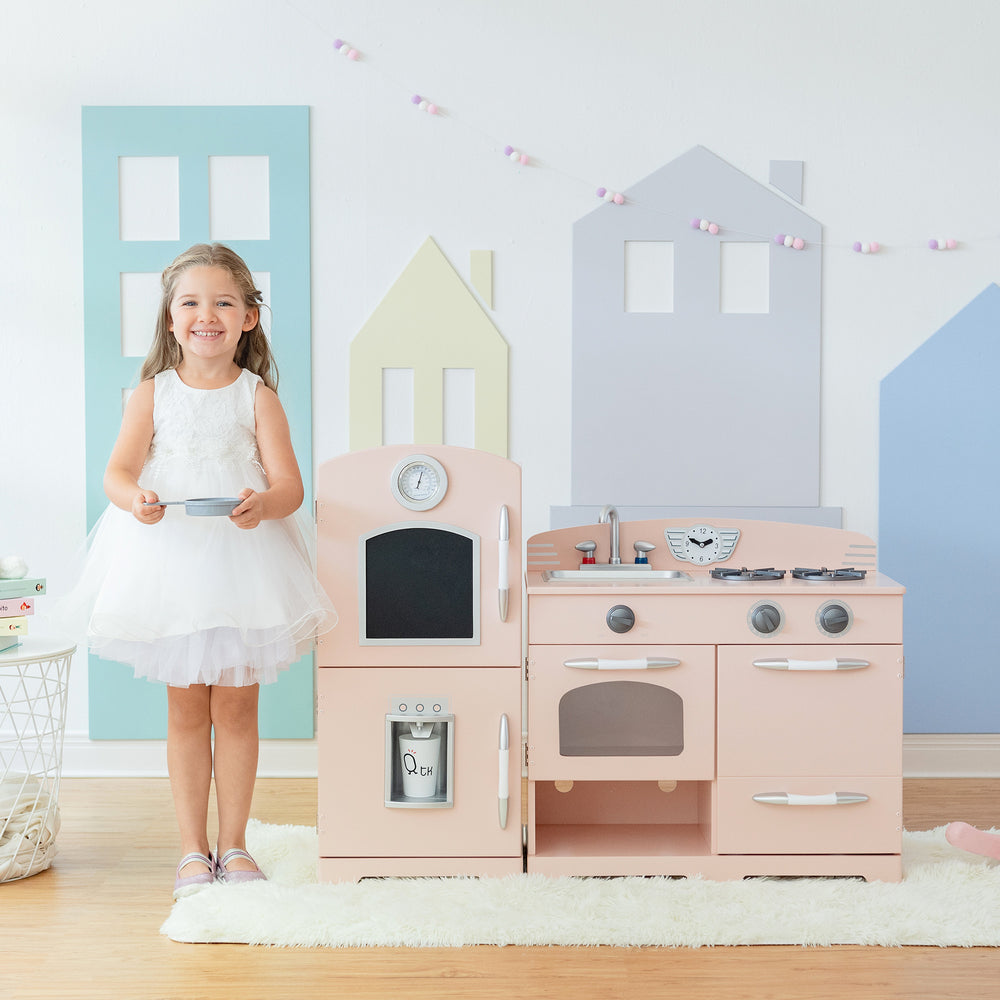 Young girl smiling in a playroom with a Teamson Kids Little Chef Fairfield Retro Kids Kitchen Playset with Refrigerator, Pink.