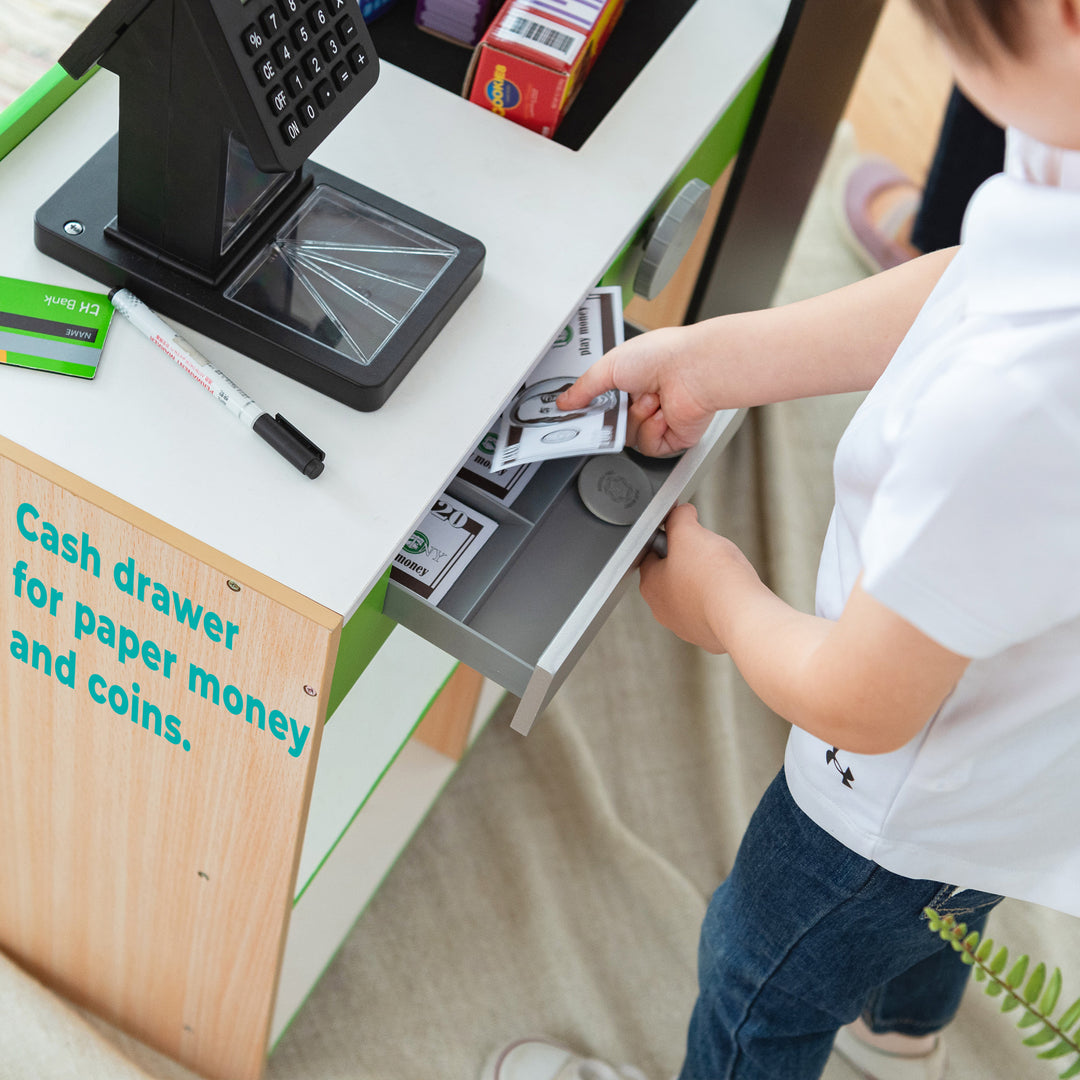 A boy puts dollar bills into the register, text on image reads "cash drawer for paper money and coins."