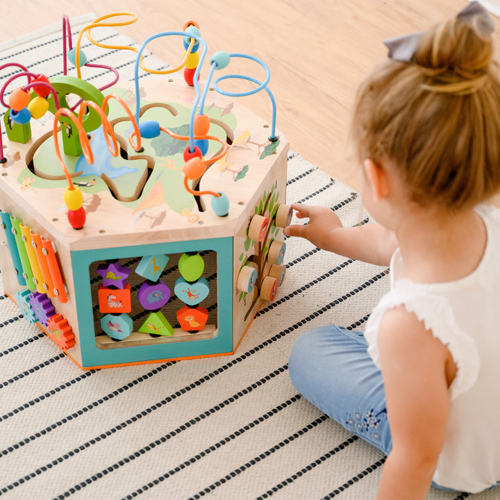 A young child playing with a Teamson Kids Preschool Play Lab 7-in-1 Large Wooden Activity Station.