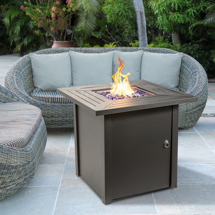 A Teamson Home Outdoor Square 30" Propane Gas Fire Pit with Steel Base with a lit flame, set in a cozy outdoor patio seating area.