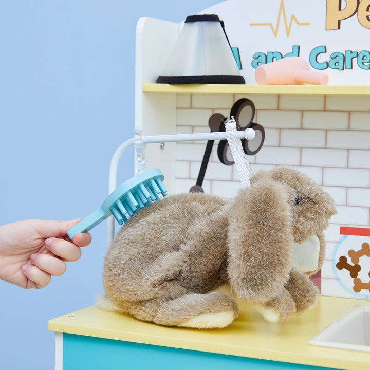 A person is brushing a plush bunny on a Teamson Kids Little Helper Wooden Pet Care and Veterinary Clinic Playset on a kids play vet clinic.
