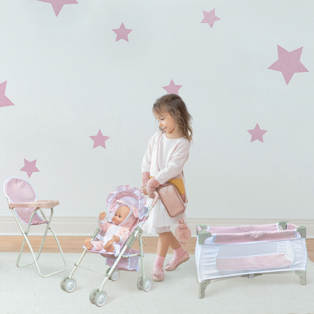 A little girl pushing a pink and white baby doll stroller between a high chair and play pen.'