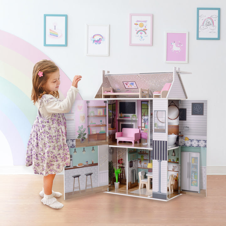 A little girl in a floral dress stands next to the 3-story dollhouse open revealing the fully illustrated interior.