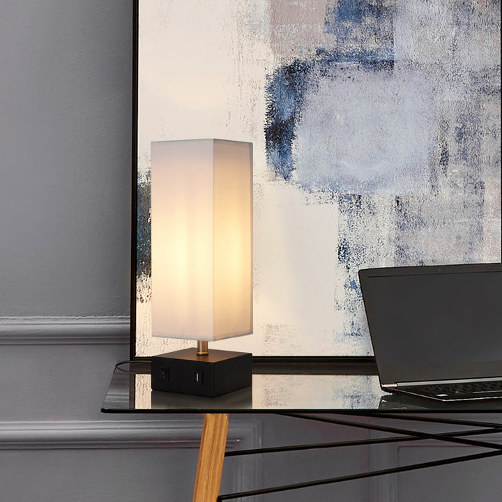 A square table lamp with a white linen like shade on a black square base.