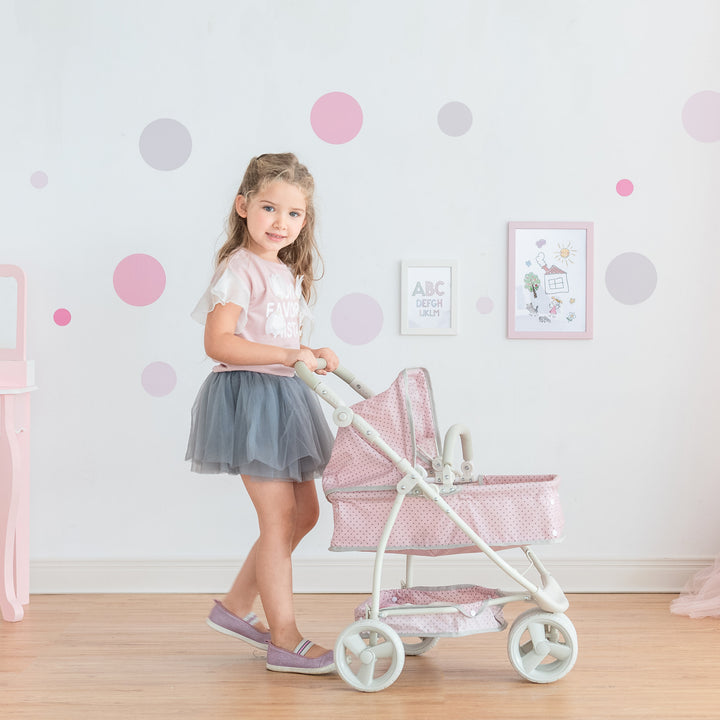 A little girl pushing a Olivia's Little World Polka Dots Princess 2-in-1 Baby Doll Stroller, Pink with an adjustable handle in a room with polka dots.