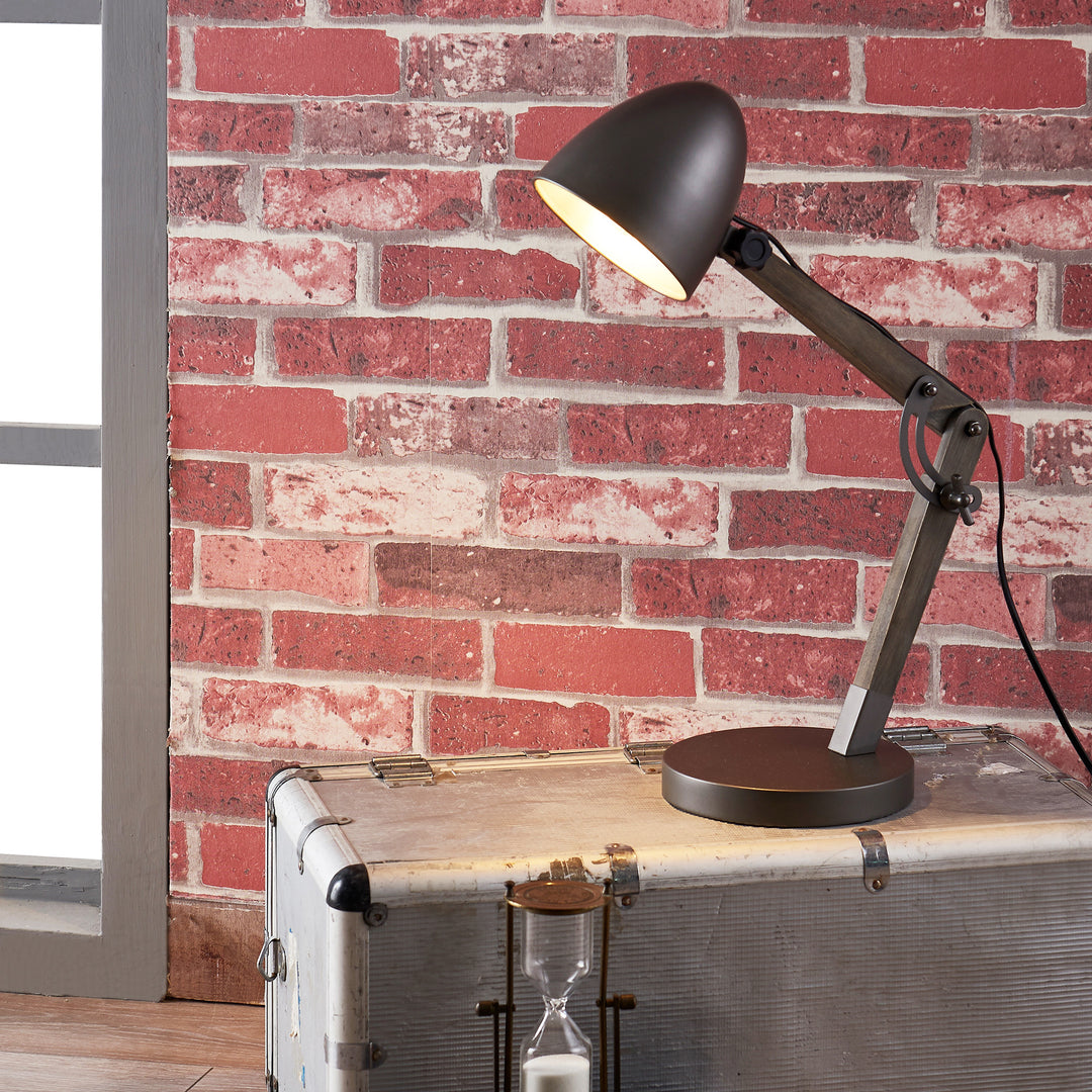 A Teamson Home Lexi Modern Reading Table Lamp with Black Shade and Brushed Steel Finish on top of a suitcase in front of a brick wall.