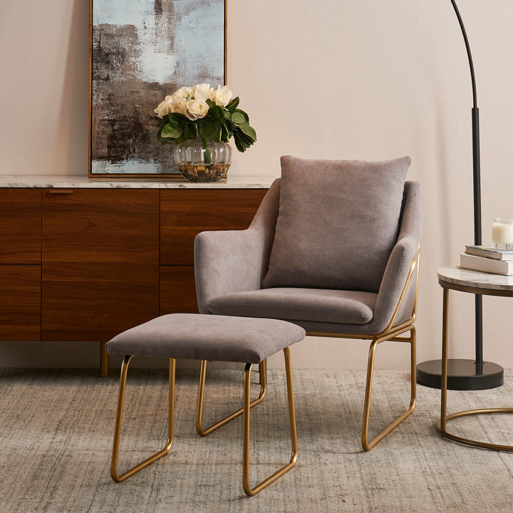Miller gray armchair and ottoman with gray fabric and gold framework next to a sideboard an floor lamp.
