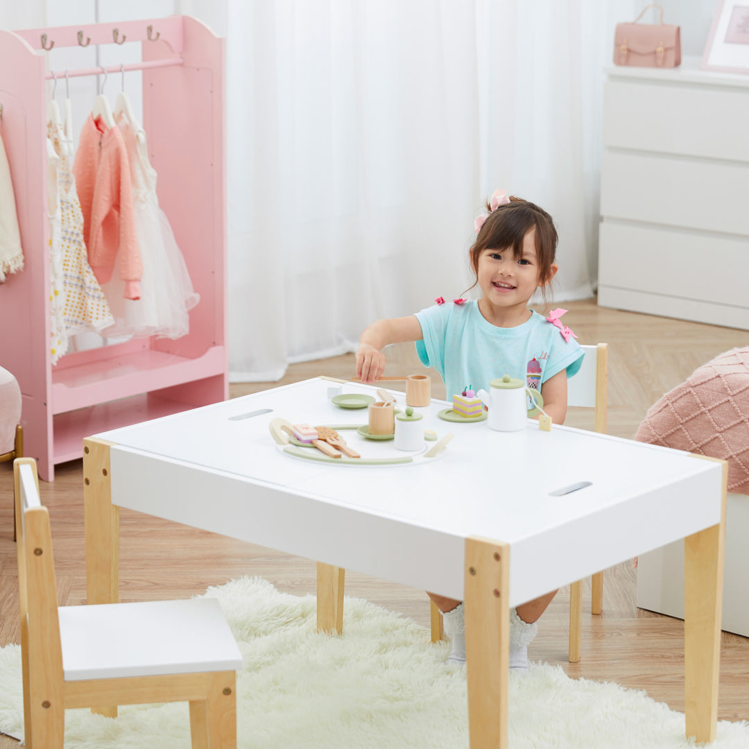 A little girl sitting at a white and wood child-sized table in a playroom.