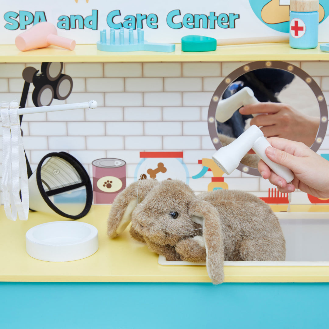 A child's hand pretends to wash a toy rabbit at the Teamson Kids Little Helper Wooden Pet Care and Veterinary Clinic Playset.