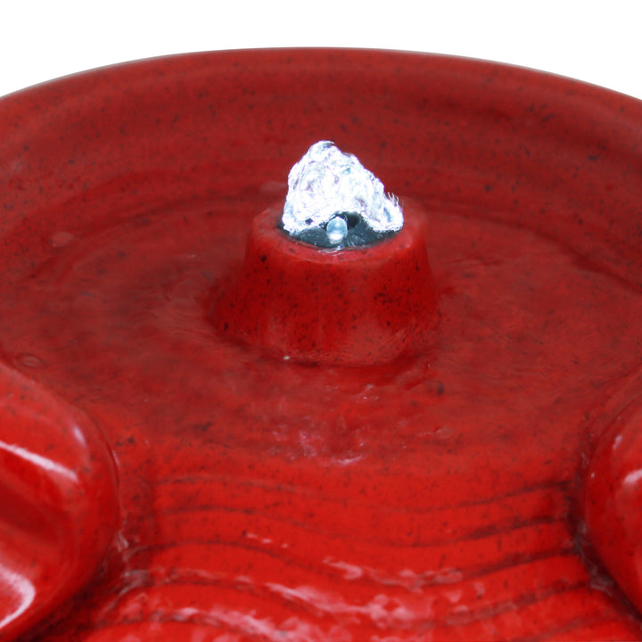 A close-up of a Teamson Home Outdoor Glazed Pot Floor Fountain with LED Lights in red ceramic surface with a small water jet on top.