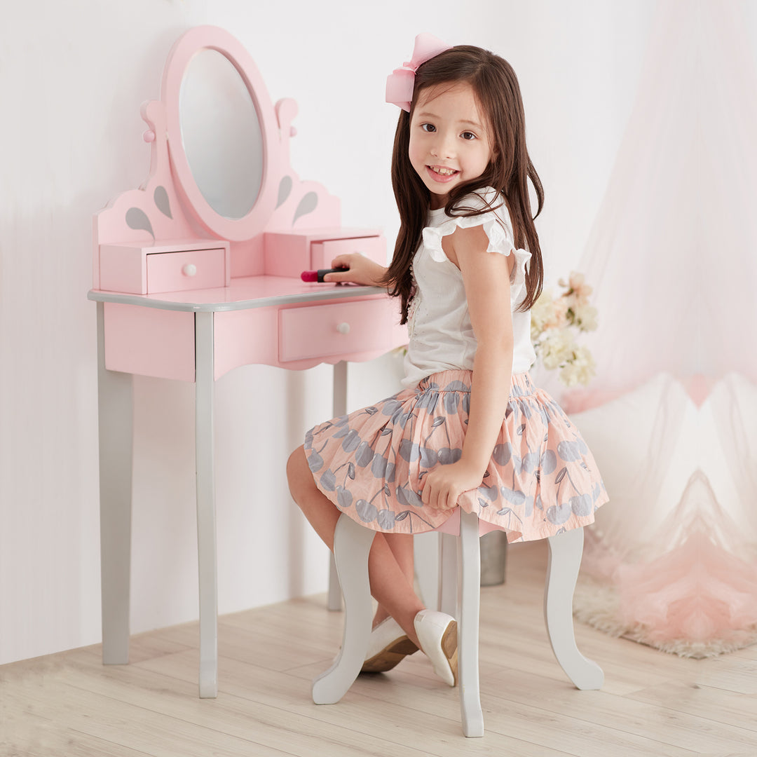 A little girl sitting on a pink Teamson Kids Little Princess Rapunzel Vanity Playset stool in front of a mirror.