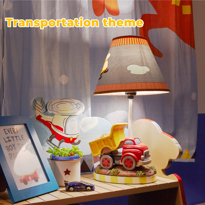 A picture of the dump truck table lamp on a shelf next to a plant and infront of a curtain with a helicopter on it.