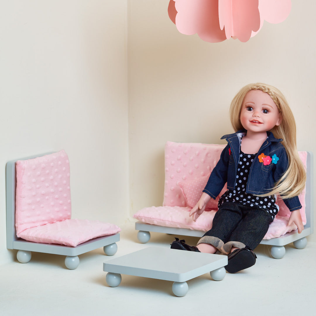 An 18" doll sitting on a couch with pink textured cusions.