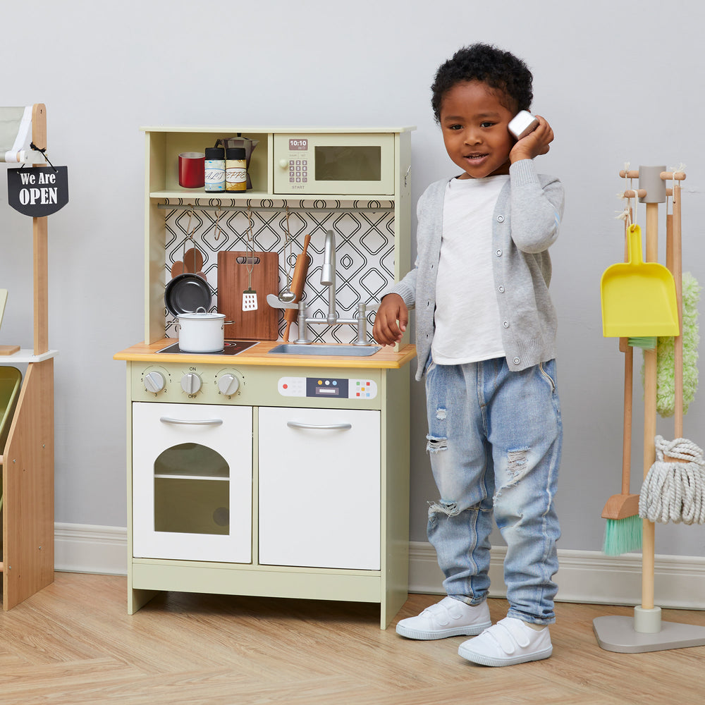 A little boy making a pretend phone call next to his Little Chef Boston Farmhouse Wooden Kitchen Playset, Green/White