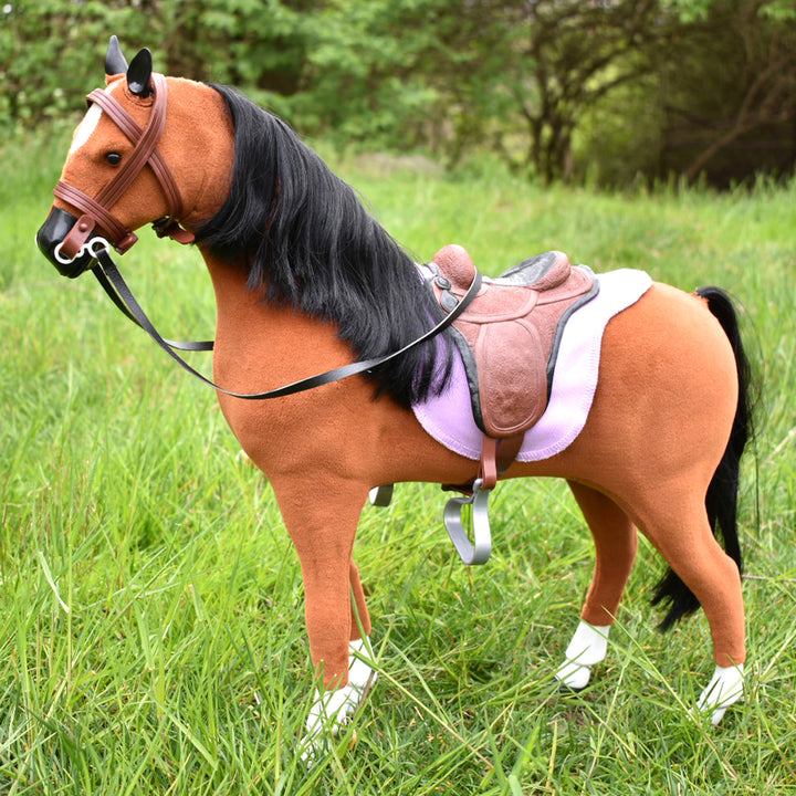 A Sophia's Doll Sized Horse and Accessories Set standing in a grassy field with an equestrian riding accessory.