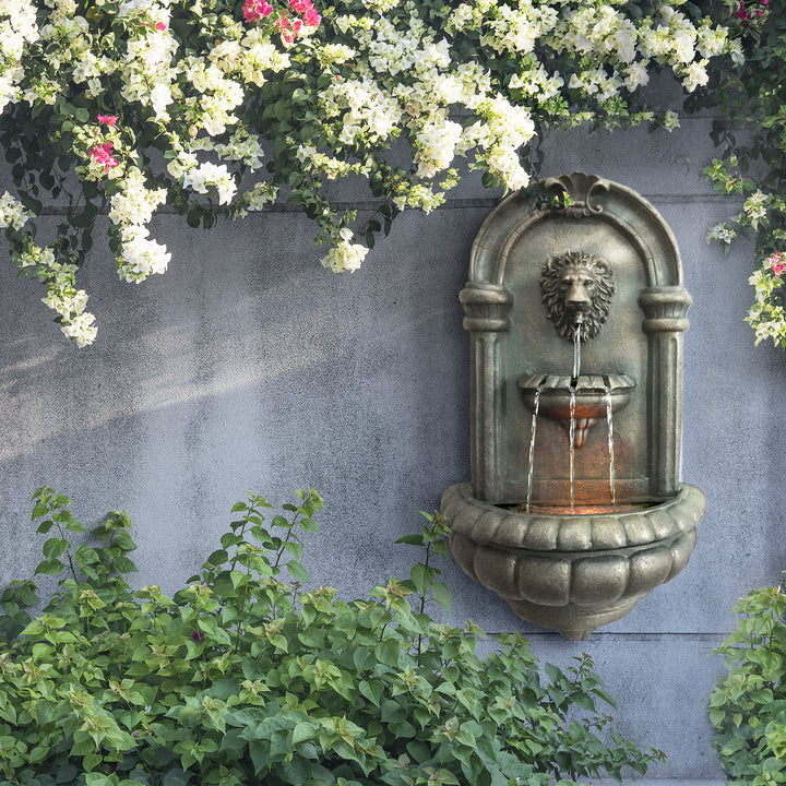 Teamson Home Outdoor Tiered Lion Head Wall Water Fountain mounted on a wall underneath pink and white flowering tree