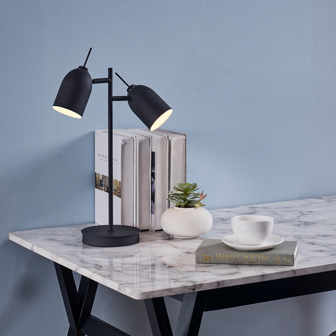 Teamson Home's Mason Modern Adjustable Double Light Table Lamp, Black, on a desk with a plant, books and a cup of tea.